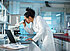 Frau mit weißem Kittel schaut in einem Labor durch ein Mikroskop