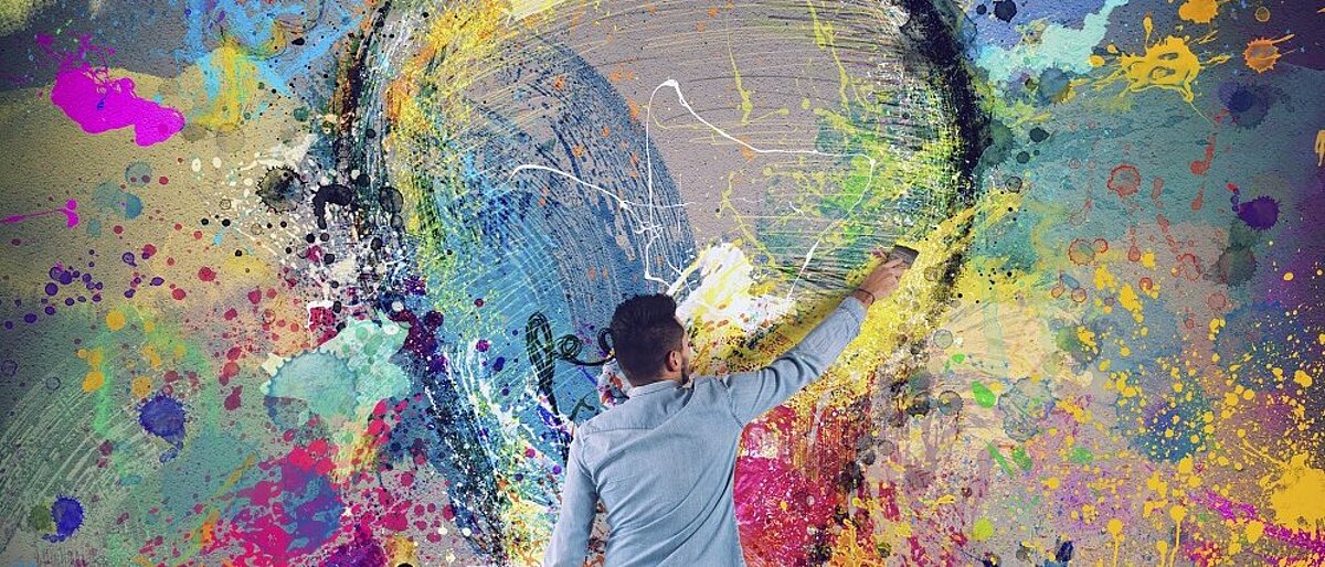 Junger Mann malt mit bunter Farbe eine Glühbirne an eine Wand