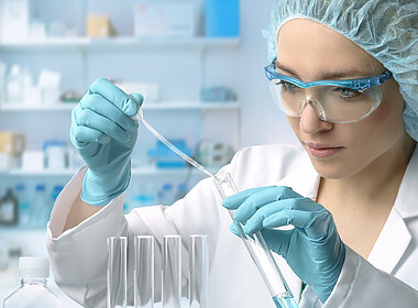 Frau mit Schutzkleidung und Reagenzglas in einem medizinischen Labor