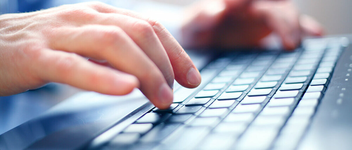 Nahaufnahme eines Mannes der mit zwei Händen auf einer Tastatur tippt