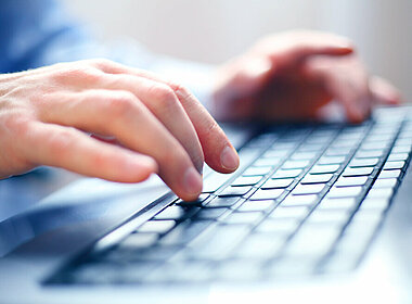 Nahaufnahme eines Mannes der mit zwei Händen auf einer Tastatur tippt