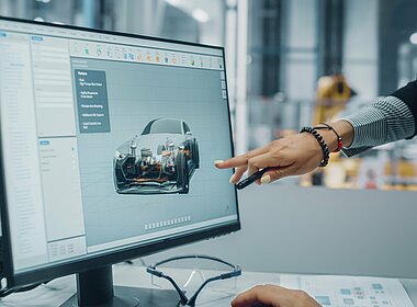 Zwei Automobil-Ingenieure diskutieren Concept Car Blueprints auf Desktop-Computer in modernen Büros in Montagewerken. Female Industrial Project Manager spricht bei der Fahrzeugfabrik mit dem männlichen Designer.