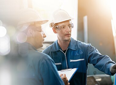Zwei Arbeiter in Arbeitsmontur mit Helm schauen sich eine Maschine an